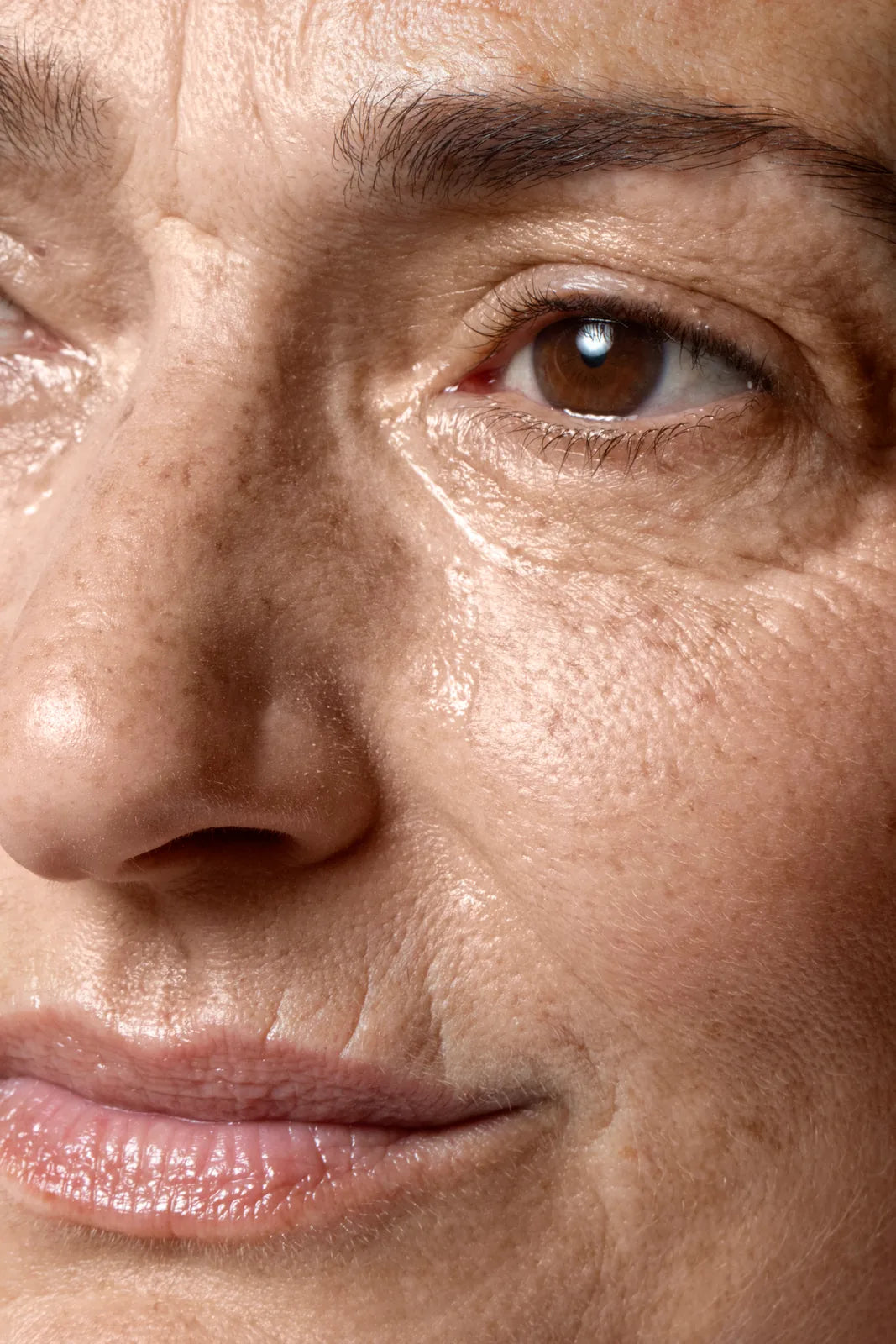 Close-up of a woman's cheek and eye area showing natural skin texture, visible pores and fine lines