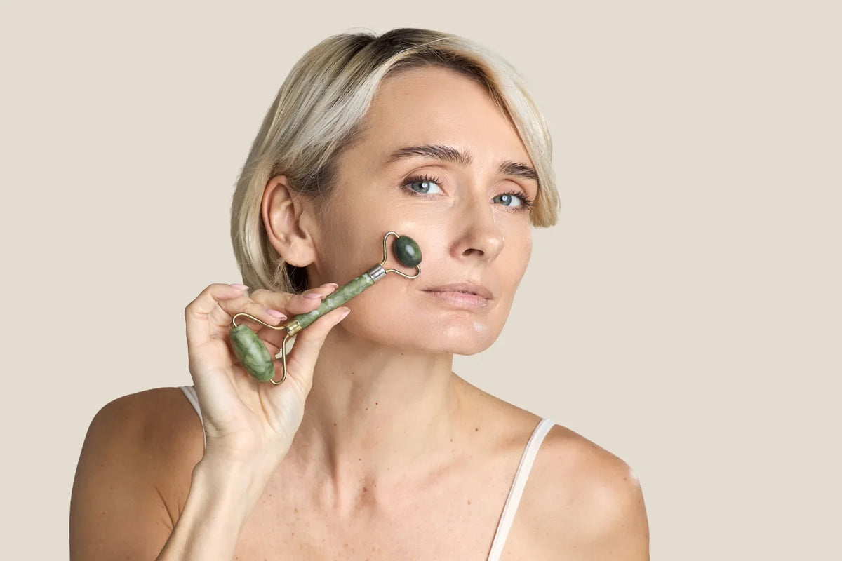 Woman in her forties rolling a cool jade facial roller under her eye and across her cheek