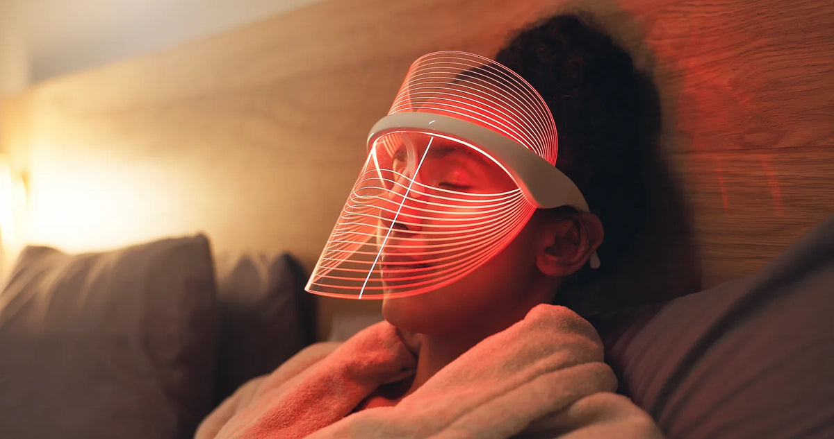 Woman resting in bed at home wearing a clear LED face shield that glows with red light