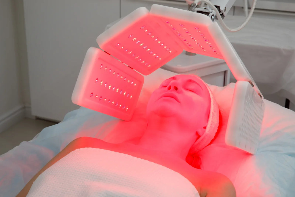Woman in her fifties relaxing under a red LED light therapy panel during a facial session